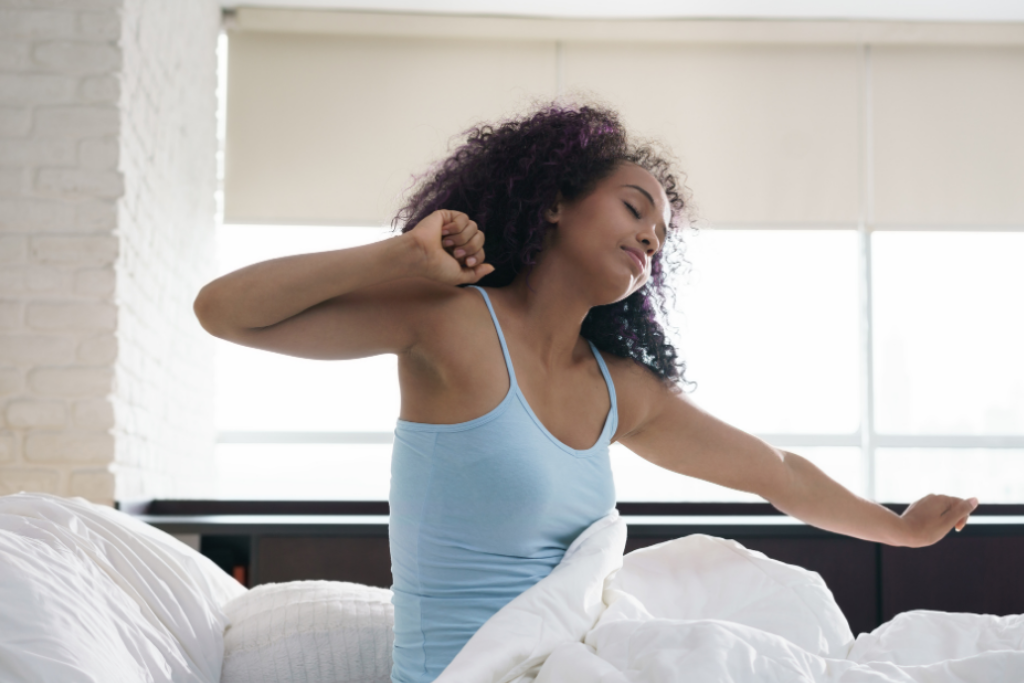 mulher despertando tranquilamente de seu sono, espreguiçando-se na cama com persiana blackout ao fundo