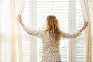 mulher em sua casa abrindo suas cortinas em ambiente integrado