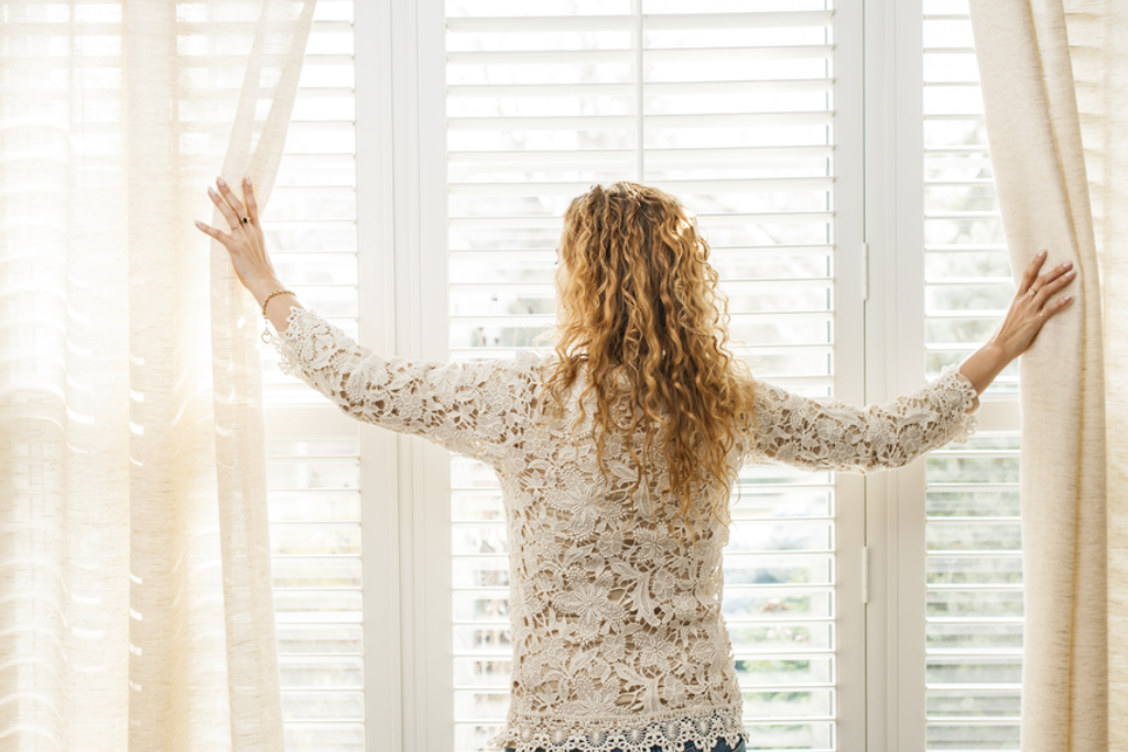 mulher em sua casa abrindo suas cortinas em ambiente integrado