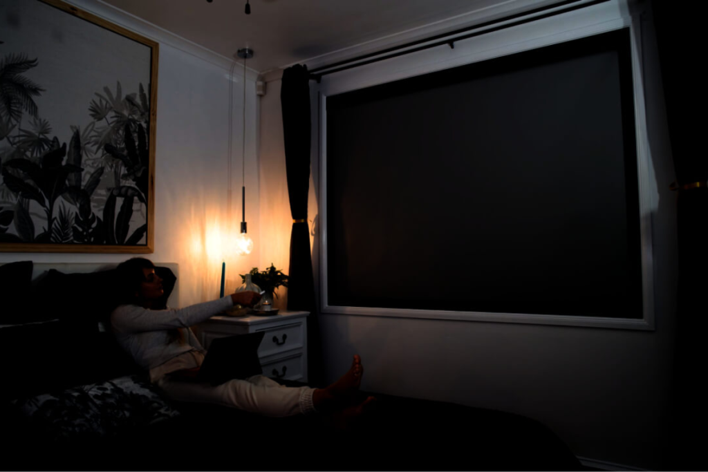 exemplo de diferença entre persiana tela solar e blackout: mulher em uma sala escurecida pela persiana blackout 